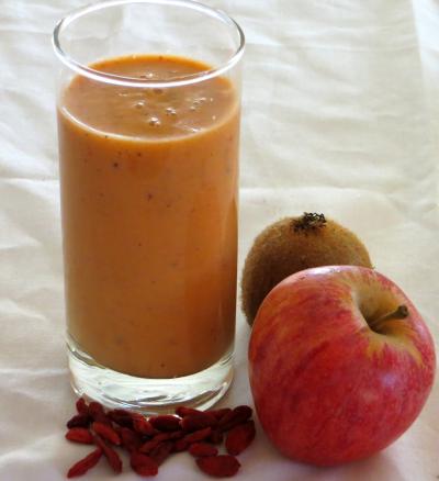 Copo com batido de iogurte e fruta, acompanhado de uma ma��, um quivi e um punhado de bagas gojis